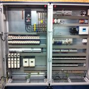 Open electric control cabinet showing circuit breakers, terminal blocks, and control modules with wiring harnesses inside an industrial panel.