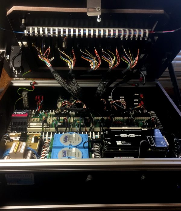 Open electronics cabinet exposing dense wiring, circuit boards, and blue modules in a control system edge.