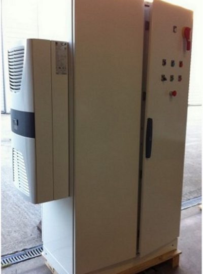 Tall beige electrical cabinet with a side control panel and red emergency-stop button, mounted on a wooden pallet in a workshop.